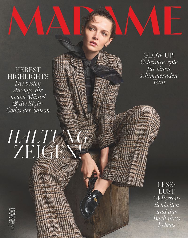 Model wearing a brown plaid suit and black neck scarf seated on a wooden block for Madame Germany magazine cover.