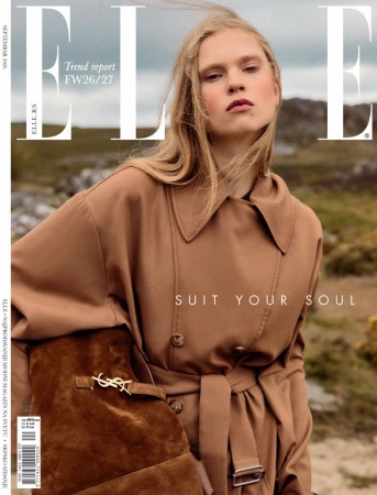 Model Vilte Seskauskyte poses in a camel trench coat with a brown suede shoulder bag for an Elle magazine cover shoot outdoors.