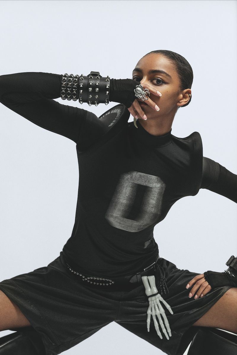 Fashion shot of a model wearing a black outfit with silver accents against a stark white background, showcasing edgy and modern style.