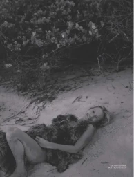Kate Moss smiles while lying on sandy ground beside coastal foliage wearing a textured Bottega Veneta dress in black and white.
