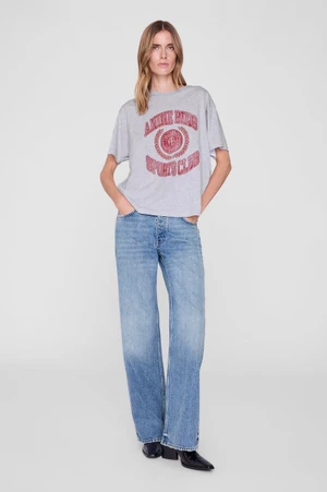 Model wearing a grey graphic t-shirt, wide-leg blue jeans, and black boots against a plain grey studio backdrop.