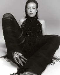 Woman in dark halter top and trousers seated against a white background for CAP 74024 project Allie x