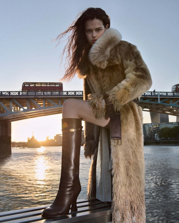 FKA Twigs wearing a furry coat and tall boots on a bridge overlooking a river for Burberry Winter 2026