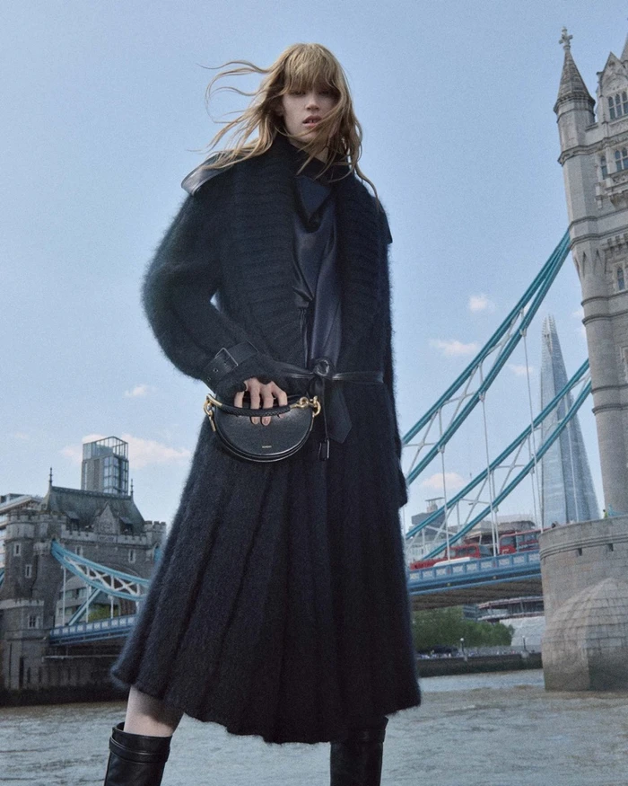 FKA Twigs wearing a long black coat and holding a black handbag near Tower Bridge for the Burberry Winter 2026 campaign.