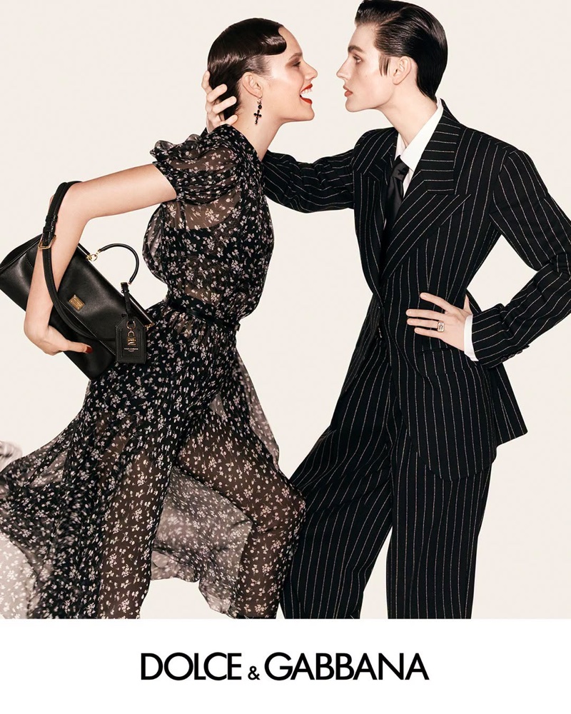 Two models posing dynamically against a light background for a Dolce and Gabbana campaign, wearing a floral dress and a pinstripe suit.