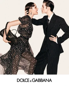 Two models posing dynamically against a light background for a Dolce and Gabbana campaign, wearing a floral dress and a pinstripe suit.