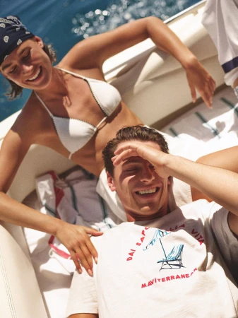 Smiling couple on a boat: woman in white bikini and bandana, man in t-shirt, enjoying a sunny day on the water.