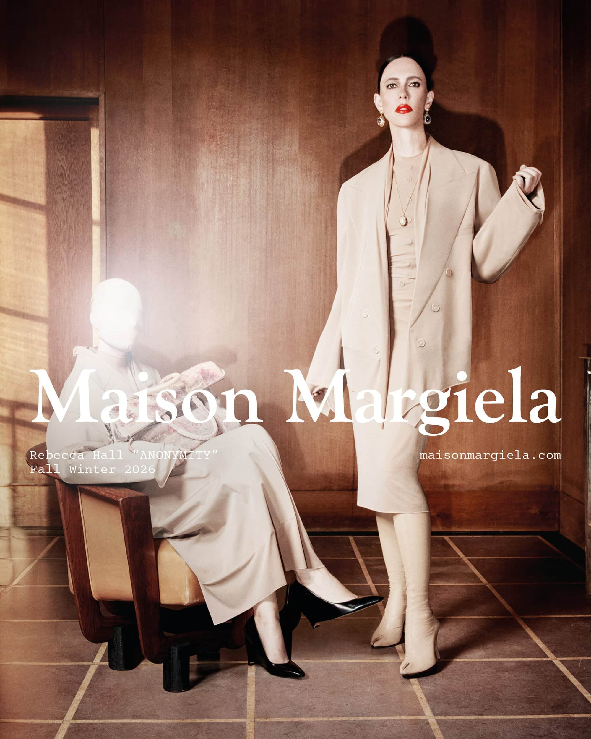 Rebecca Hall wearing a tailored beige skirt suit standing beside a seated veiled figure in a wood-paneled room for Maison Margiela.