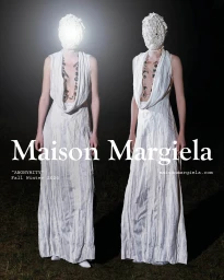 Two figures in textured white face coverings and draped white gowns standing against a dark outdoor night background.