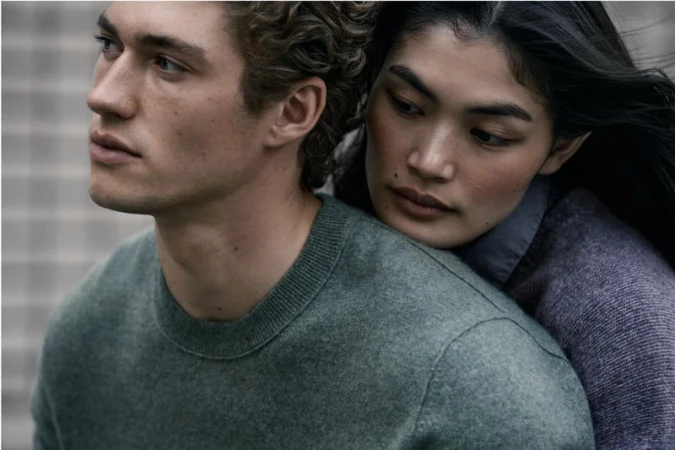 Close-up of a woman leaning against a man wearing a green knit crewneck sweater.