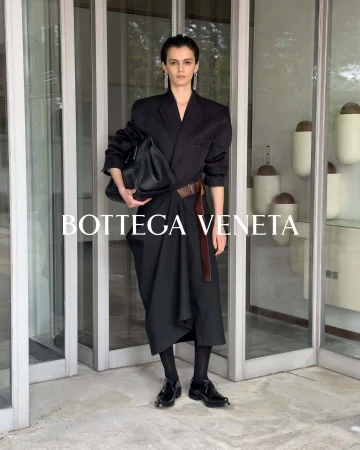 Model Sihana Shalaj posing in a black tailored wrap dress with a brown belt for the Bottega Veneta Winter 2026 ad campaign.