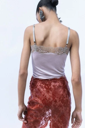 Model seen from the back wearing a pale mauve lace-trimmed camisole top and sheer rust lace skirt against a white backdrop.