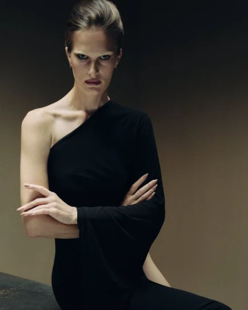 Model wearing a black one-shoulder dress with arms crossed against a dark gradient studio background