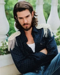 Andrew Garfield with a beard wearing a dark plaid shirt with embellished epaulets and blue jeans
