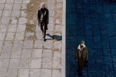 High angle shot of two male models in designer outerwear walking on split stone paved surfaces in contrasting light and shadow.