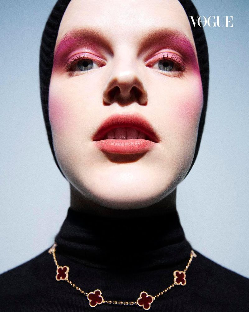 Model Hannah Motler with vibrant pink eyeshadow wearing a black balaclava and gold clover motif necklace for Vogue Thailand.