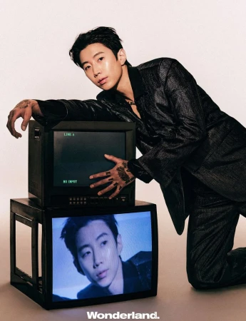 Jay Park leaning over stacked vintage CRT television monitors wearing a dark textured suit against a neutral studio backdrop.