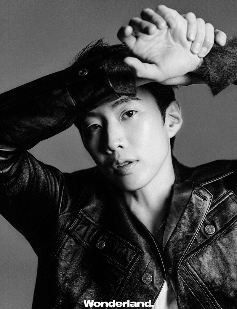 Monochrome portrait of musician Jay Park wearing a black leather jacket with his hands raised to his forehead against a studio backdrop.
