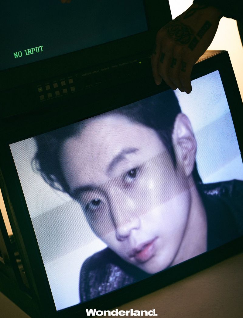 Close-up portrait of Jay Park displayed on a video monitor screen with a tattooed hand holding the black frame.