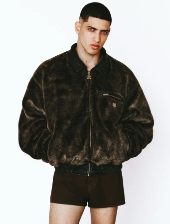 A man in a plush dark brown bomber jacket and matching shorts posing against a seamless white studio background.