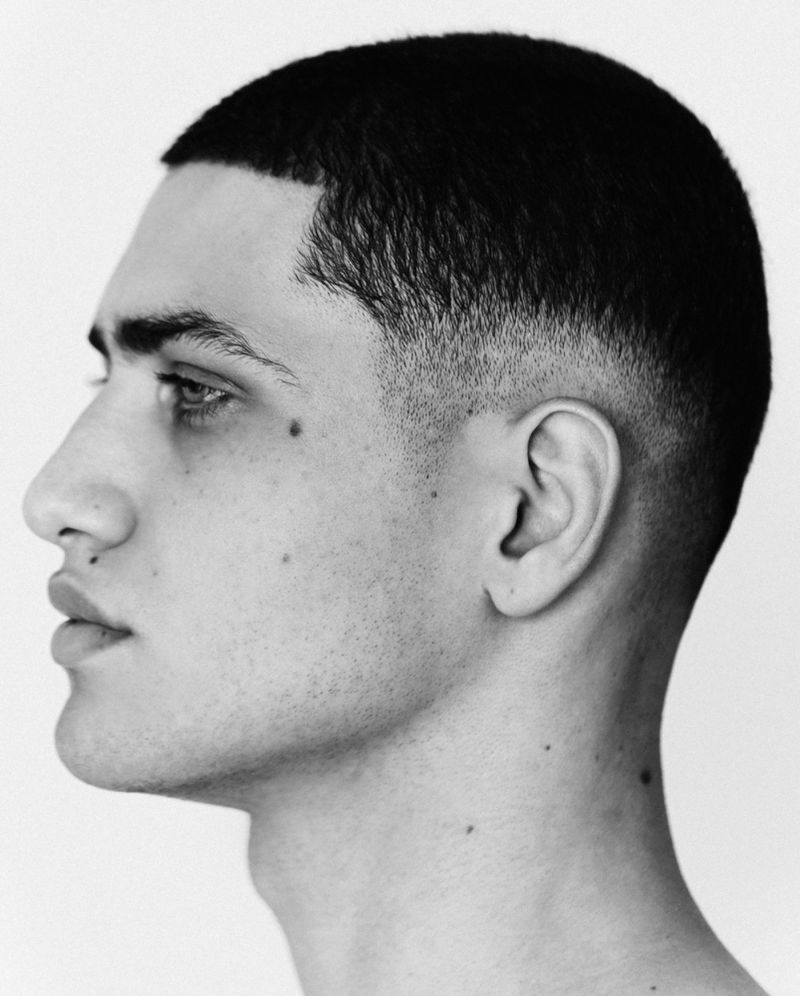 Black and white side profile portrait of a young man with a short fade haircut against a white background.