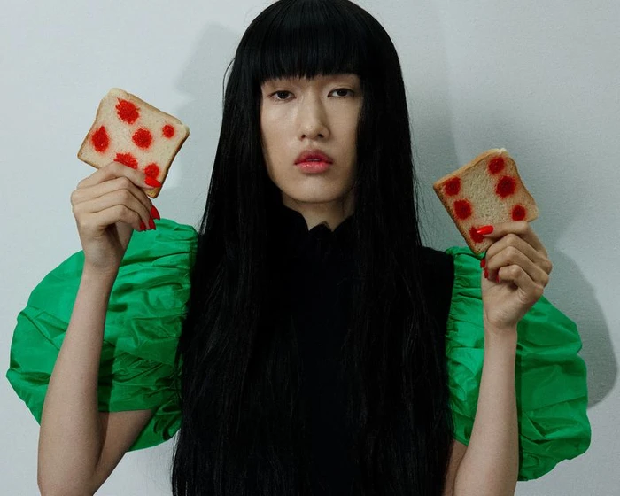 Model Asako Sato in puff green sleeves holding two slices of bread with red polka dots against a plain light wall.