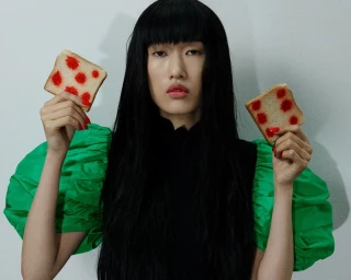Model Asako Sato in puff green sleeves holding two slices of bread with red polka dots against a plain light wall.