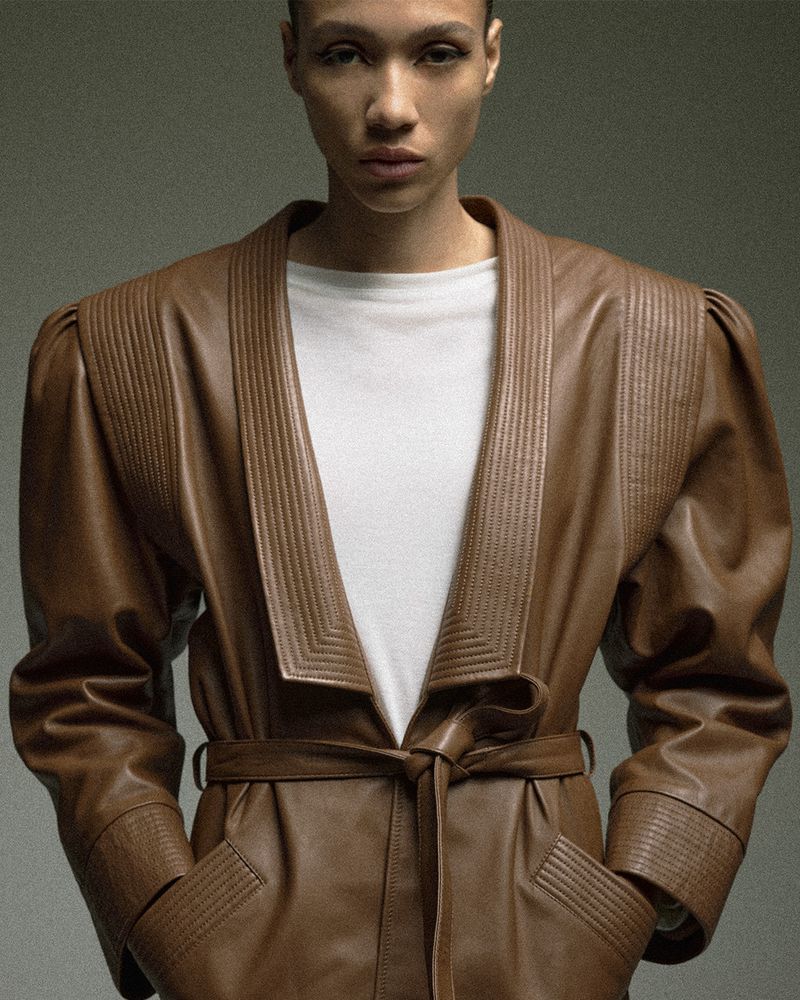 Model Mauria Caetano wearing a belted brown leather coat with wide lapels over a white shirt for Harper's Bazaar France.