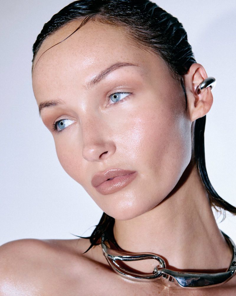 Close-up beauty portrait of a woman with slicked-back hair wearing a sculptural silver necklace and ear cuff.