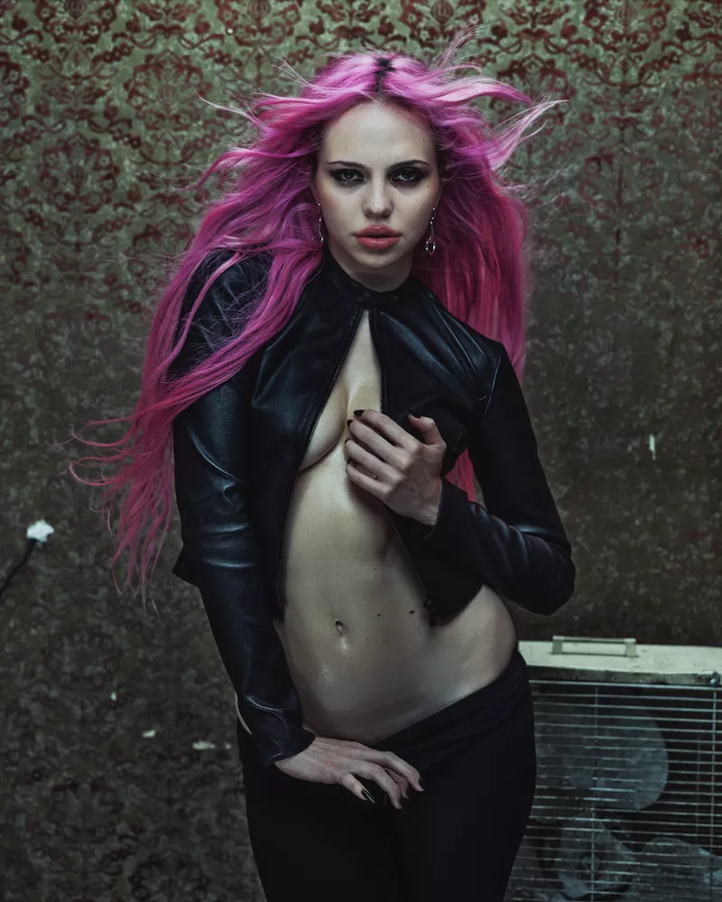 Adéla Jergová with bright pink hair wearing an open black leather jacket against a patterned backdrop for V Magazine.