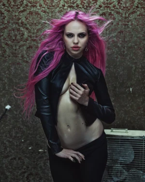 Adéla Jergová with bright pink hair wearing an open black leather jacket against a patterned backdrop for V Magazine.