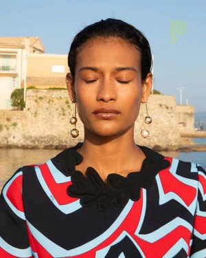 Model Mar G with eyes closed wearing a graphic red, blue, and black print top and gold drop earrings in Saint-Tropez.