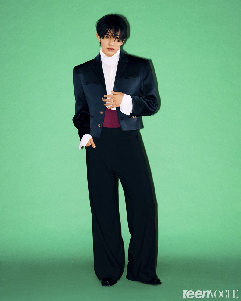 K-pop soloist Evan posing against a vivid green backdrop in a cropped black blazer, white collared shirt, and wide-leg trousers.