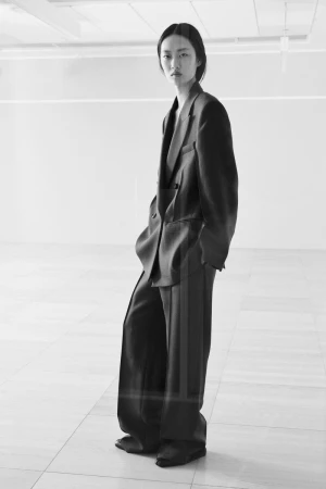 Model Ruiyi Zhang poses in an oversized dark tailored pantsuit in a bright minimalist interior space.