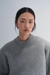 Model Ruiyi Zhang wearing a grey textured knit crewneck sweater against a neutral studio backdrop for H&M.