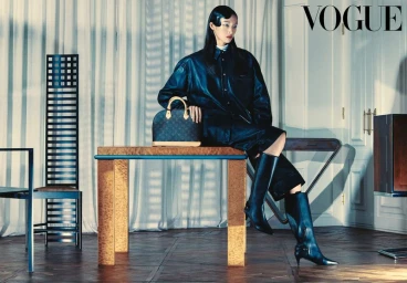 Model Shiqi Fang in an oversized black leather jacket and boots seated on a table next to a monogram handbag for Vogue Korea.
