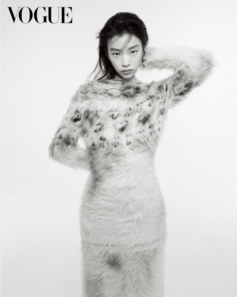East Asian woman posing in a fuzzy textured patterned dress with one hand behind her head against a plain white background.