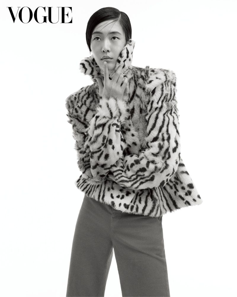 Model posing in a patterned high-collar fur jacket and wide trousers against a pure white seamless studio backdrop.