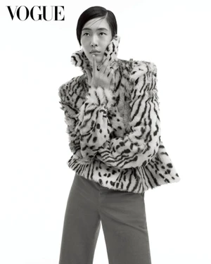 Model posing in a patterned high-collar fur jacket and wide trousers against a pure white seamless studio backdrop.