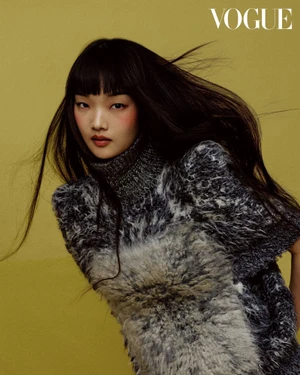 East Asian model with straight bangs wearing a fuzzy grey high-neck knit top against a yellow-green backdrop.