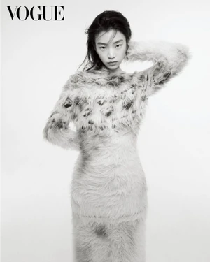 East Asian woman posing in a fuzzy textured patterned dress with one hand behind her head against a plain white background.