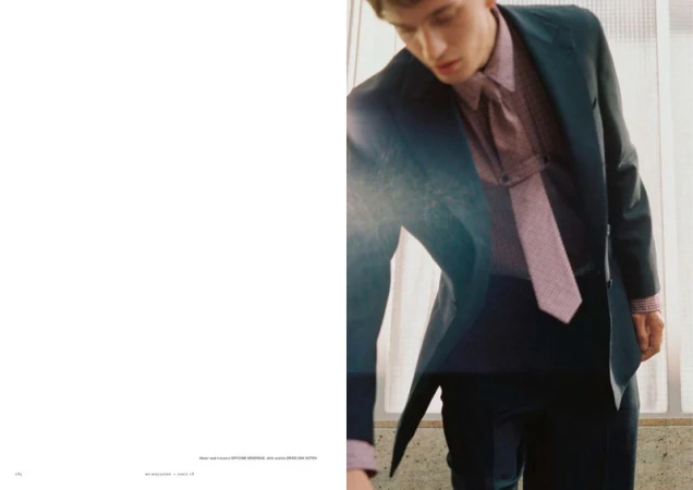 Fashion editorial spread of a man leaning forward wearing a dark suit, patterned shirt, and matching necktie beside white negative space.