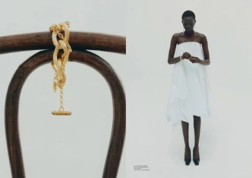 Diptych with a gold chain bracelet on a bentwood chair beside a Black woman model in a sculptural white strapless dress against a white studio background.