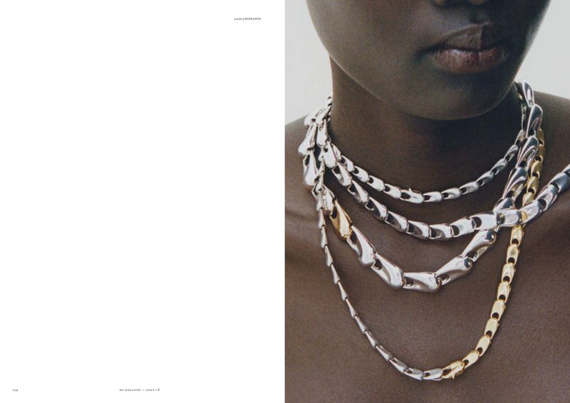 Close-up portrait of a Black woman wearing layered sculptural silver and gold chain necklaces on an editorial magazine spread.