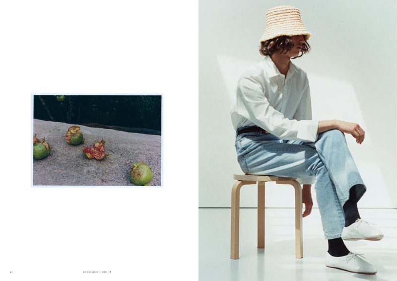 Model wearing a straw bucket hat, white button-up shirt, and light blue jeans seated on a wooden stool in a fashion editorial layout.