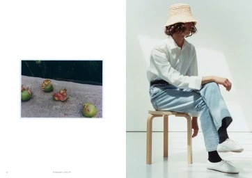 Model wearing a straw bucket hat, white button-up shirt, and light blue jeans seated on a wooden stool in a fashion editorial layout.