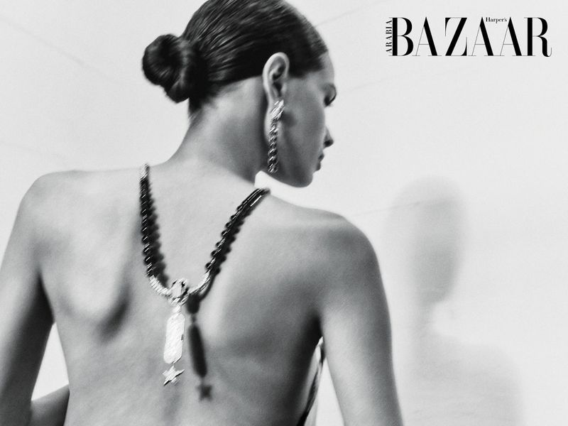 Black and white back view of a woman wearing a beaded drop necklace draped down her bare back with hair in a sleek bun.