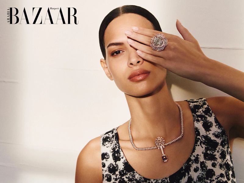Model covering one eye with a large floral ring while wearing a diamond drop necklace for Harper's Bazaar Arabia.