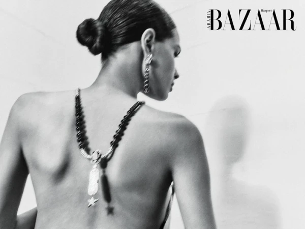 Black and white back view of a woman wearing a beaded drop necklace draped down her bare back with hair in a sleek bun.
