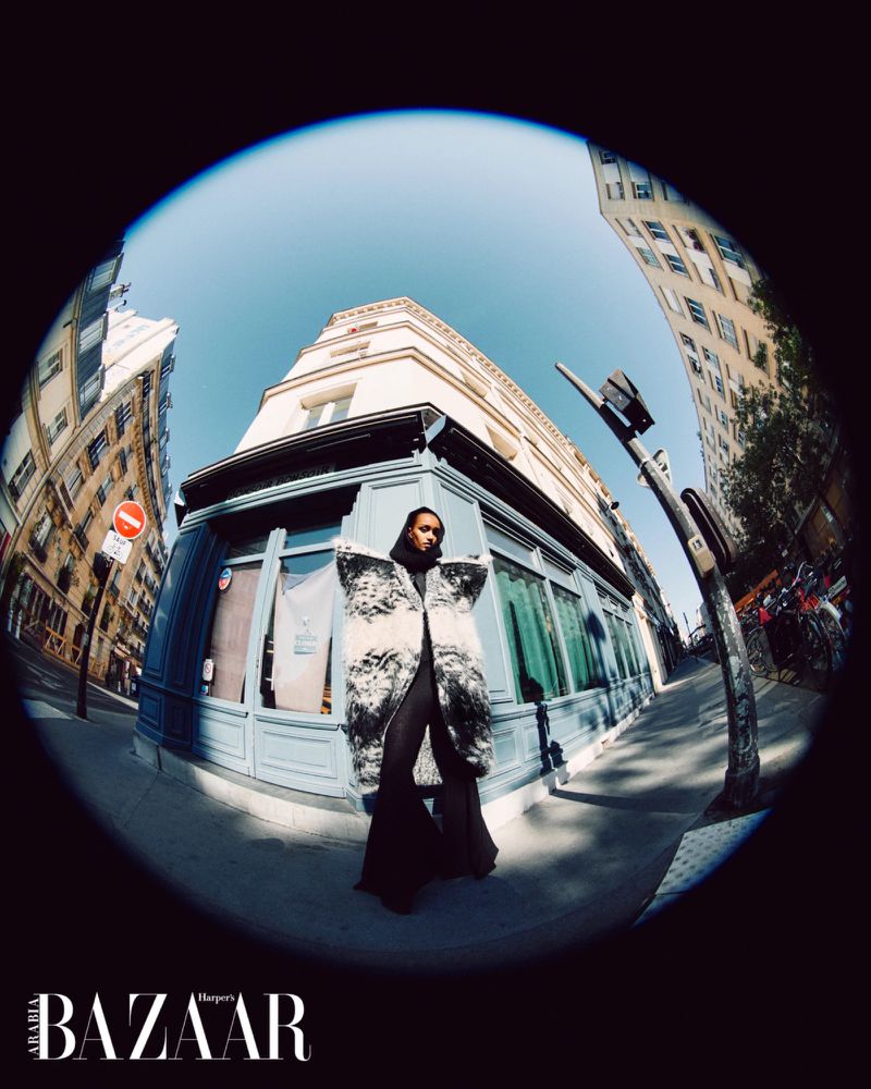 Model Muna Mahamed in an oversized black and white coat posing on an urban street corner, captured in a circular fisheye lens.